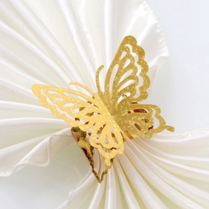Elegant gold hollow laser-cut butterfly napkin ring on white silk fabric for weddings