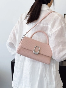 Pink textured leather crossbody bag with silver buckle worn by a model in white