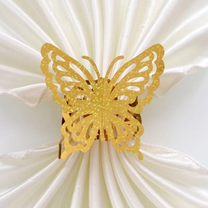 Symmetric top view of golden laser-cut butterfly napkin ring on white satin fabric