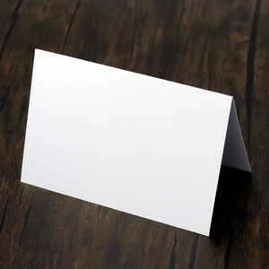 Foldable white matte paper place cards on a dark wooden table for wedding seating