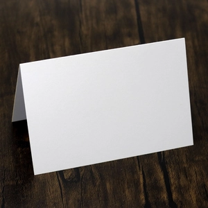 Blank white fold-over place cards for weddings on a dark wood grain background surface