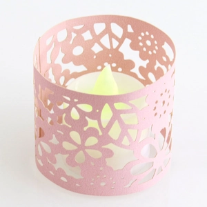 Macro detail of laser-cut paper candle sleeve with pink floral patterns and LED tea light