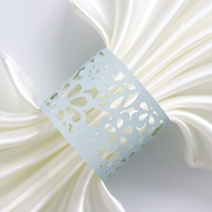 Detailed macro view of light blue laser-cut floral napkin ring on white satin fabric