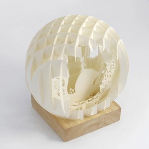 Macro detail of 3D layered paper-cut lamp featuring silhouettes and a wooden base