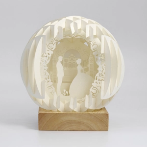 Detail of multi-layer paper-cut wedding scene with LED sphere and wooden base