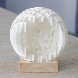 Detailed laser-cut paper deer and forest inside an LED 3D globe with wooden base