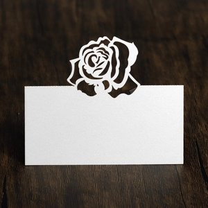 Macro view of white laser-cut rose place card with elegant hollow pattern on wood