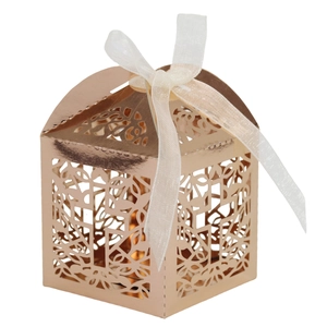Detail of rose gold laser-cut favor box with intricate hollow cross and cream ribbon