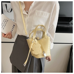 Detail of yellow crocodile pattern leather bucket bag with bear charm on a model