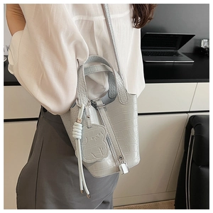 Detail of light blue crocodile pattern bucket bag with bear charm and metallic hardware