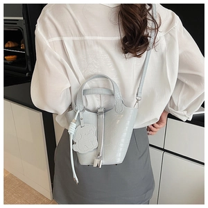 Detail of light blue croc-embossed bucket bag with silver clasp and white dog charm