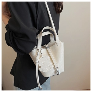 Detail of white crocodile texture bucket bag with metal lock and cute bear charm