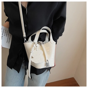 Detail view of white crocodile pattern bucket bag with cute dog charm and metal clasp