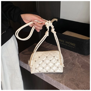 Close-up of cream quilted bag with rhinestone details and knotted cord shoulder strap