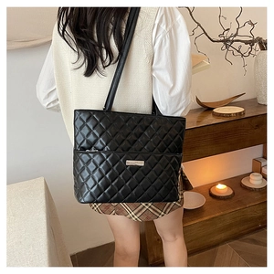 Detail of black quilted tote bag with silver metal plaque on a lifestyle background