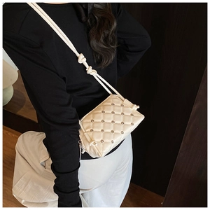 Detail of cream quilted crossbody bag featuring silver stud accents and rope shoulder strap