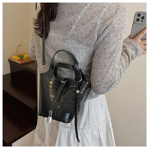 Rear view of a model wearing a mini black crocodile pattern bucket bag with a silver lock