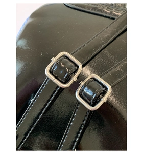 Détail de la matière en cuir noir brillant et des boucles métalliques carrées argentées