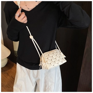 Detail of white quilted crossbody bag with silver studs and elegant chain strap on a model