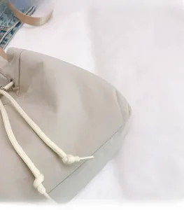 Detail view of cream nylon drawstring bag with thick cotton ropes and metal eyelets