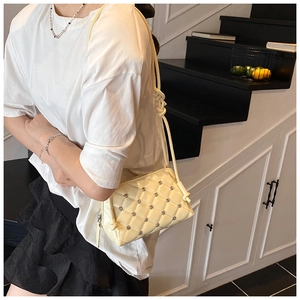 Close-up of beige quilted shell bag featuring silver stud details and knotted strap