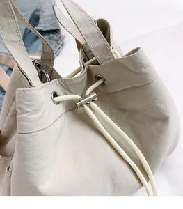 Detail of light beige nylon bucket bag featuring silver metal eyelets and drawstring cord