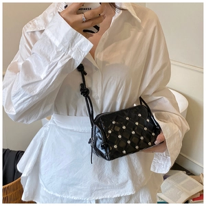 Close-up of black patent leather crossbody bag with diamond quilting and silver studs