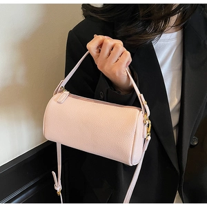 Close-up of pink lychee leather cylinder bag with gold hardware held by a model