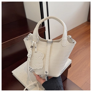 Close-up of white crocodile pattern bucket bag with silver lock and bear pendant charm