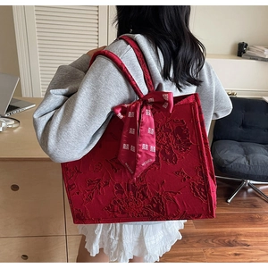 Detail of red tote bag with floral texture and silk ribbon showing a side-back view for women