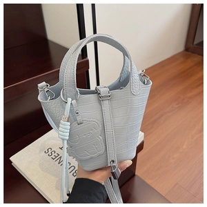 Close-up of light blue croc-embossed bucket bag with leather doll charm and metal lock