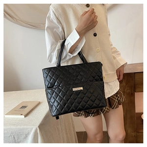 Detail of a black quilted tote bag with a metal plaque shown in a stylish lifestyle setting