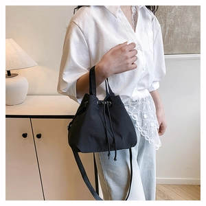 Detail of minimalist black nylon drawstring bucket bag showing adjustable shoulder strap