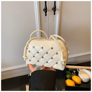 Detail of cream quilted mini crossbody bag featuring metallic stud accents and fine texture