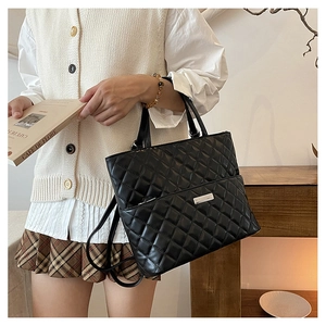 Close-up of black quilted tote bag featuring silver metal logo and dual handles