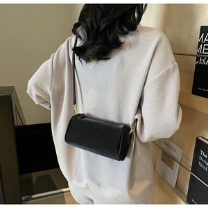 Close-up of a black textured leather cylinder bag with gold hardware worn by a model