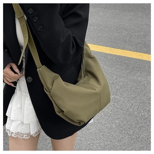 Close-up of olive green crossbody dumpling bag with pleated texture on a street model