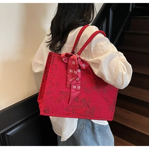 Detailed view of red wedding tote bag with floral embossing and silk bow accessory