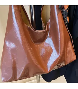 Close-up of brown glossy faux leather tote bag showing soft texture and natural folds