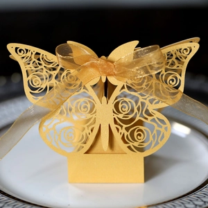 Detail of laser-cut gold butterfly candy box with rose patterns and organza ribbon