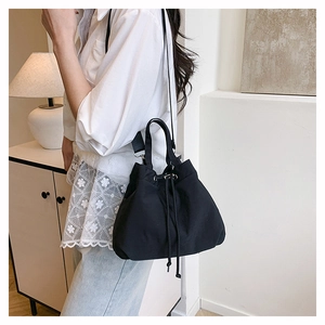 Minimalist black nylon drawstring bucket bag shown on model in a soft lit indoor setting