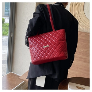 Detail of red quilted tote bag featuring a silver metal logo plate and zip closure