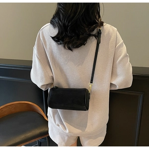 Detail of a black leather cylinder crossbody bag with golden metal hooks on a model