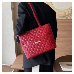Detailed view of a red quilted faux leather tote bag with silver logo on a person
