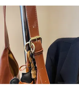 Detail of brown faux leather tote bag with gold metal buckle and woven rope charm