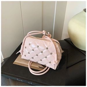 Detail of pink quilted shell bag with metallic studs and glossy finish on a book