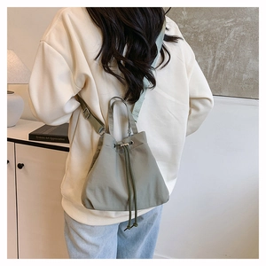 Model view of a green nylon drawstring bucket bag with adjustable straps in a minimal setting