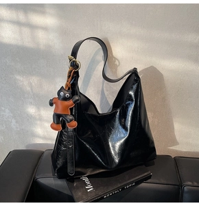 Detail of black glossy pleated hobo bag with an orange cartoon charm and magazine