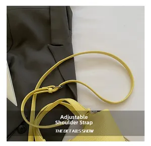 Detalle de un bolso cubo de cuero amarillo con grabado de lichi y correa ajustable