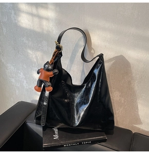 Close-up of black glossy leather tote bag with a cute cat charm on a leather chair